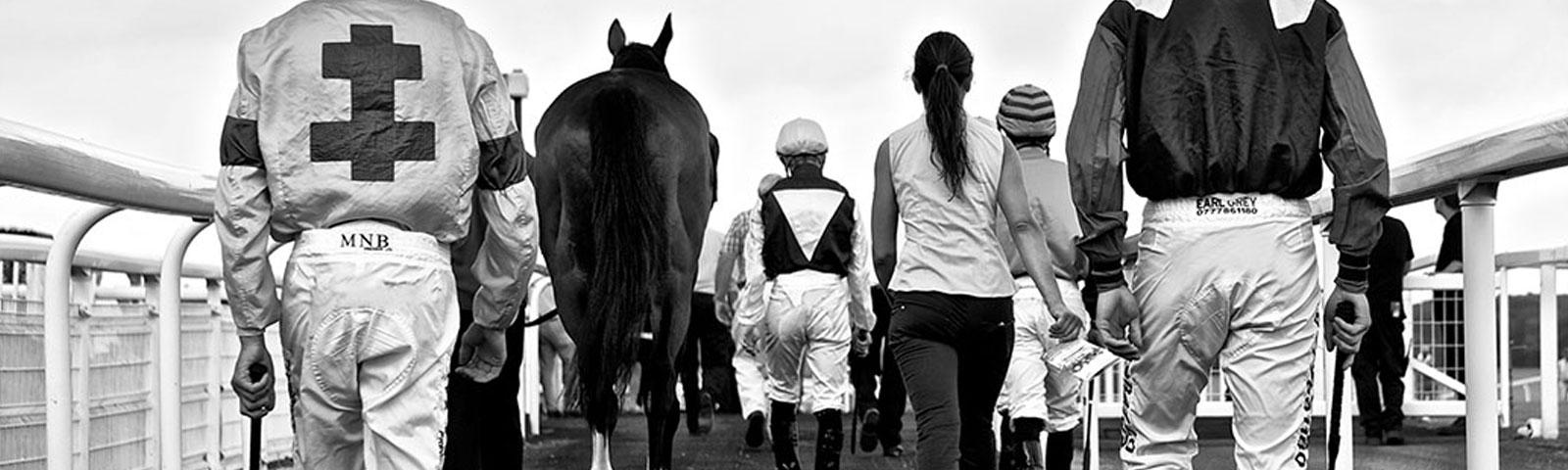 Group of jockeys walking towards a track.